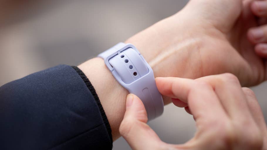 A person adjusts a purple smartwatch on their wrist outdoors.