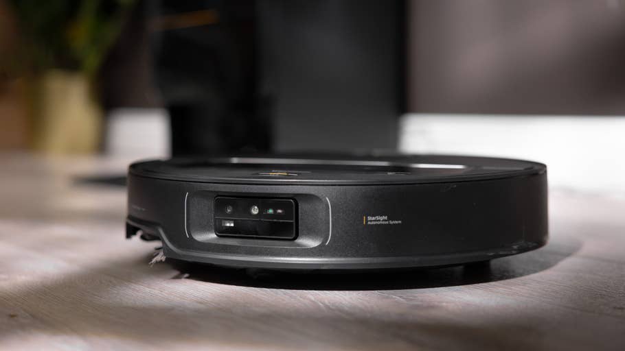 A black Roborock Saros Z70 robot vacuum cleaner on a wooden floor showing its front sensors.