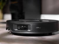 A black Roborock Saros Z70 robot vacuum on a wooden floor, showcasing its front sensors.