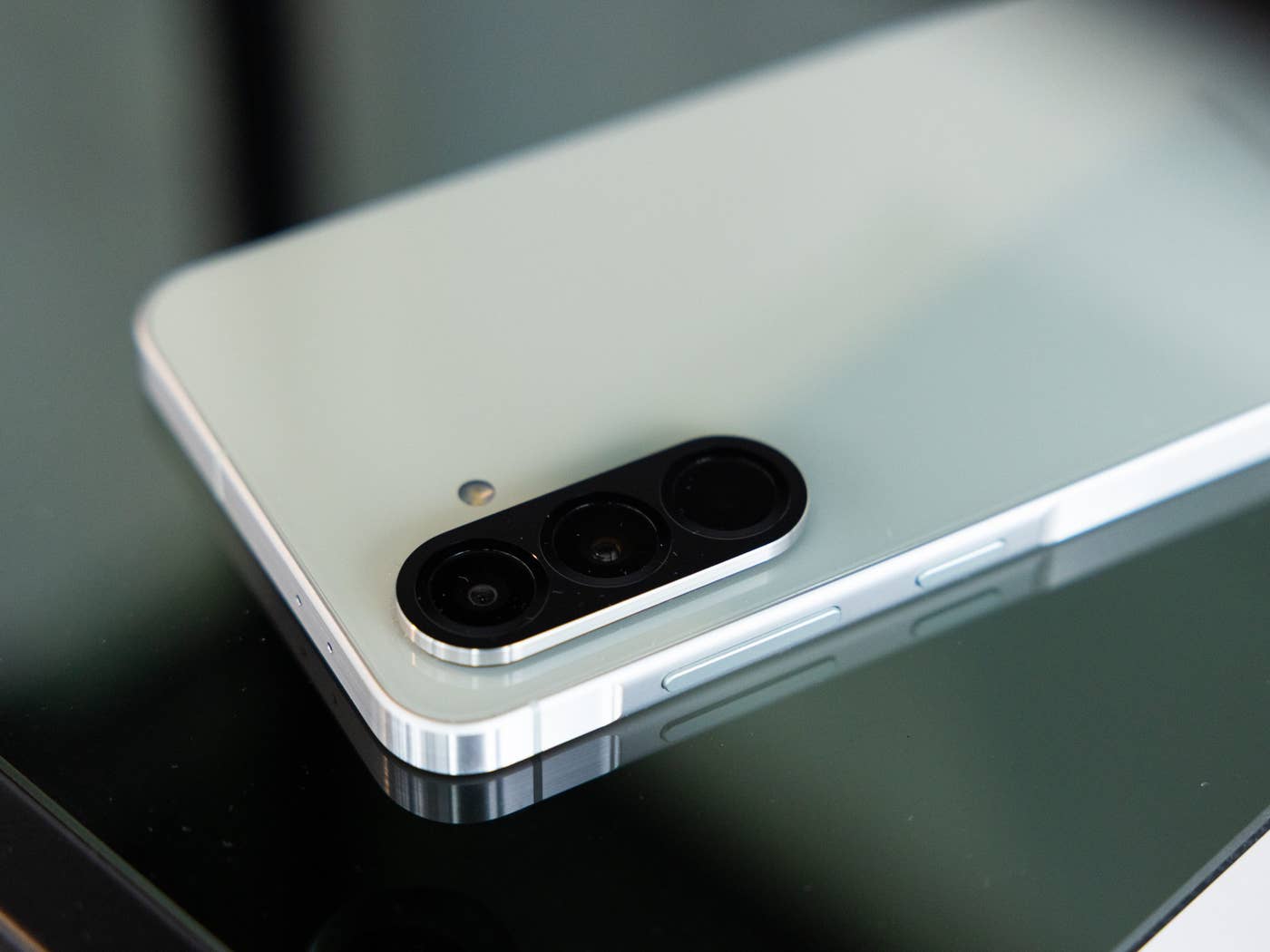 A Samsung Galaxy A56 smartphone lies on a glass surface and shows its camera module and design.