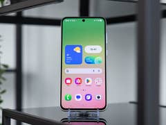 A Samsung Galaxy A series smartphone on a stand, displaying a colorful home screen with widgets.