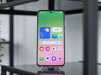 A Samsung Galaxy A series smartphone on a stand, displaying a colorful home screen with widgets.