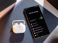 Samsung Galaxy Buds 3 charging case next to a smartphone displaying earbuds settings.