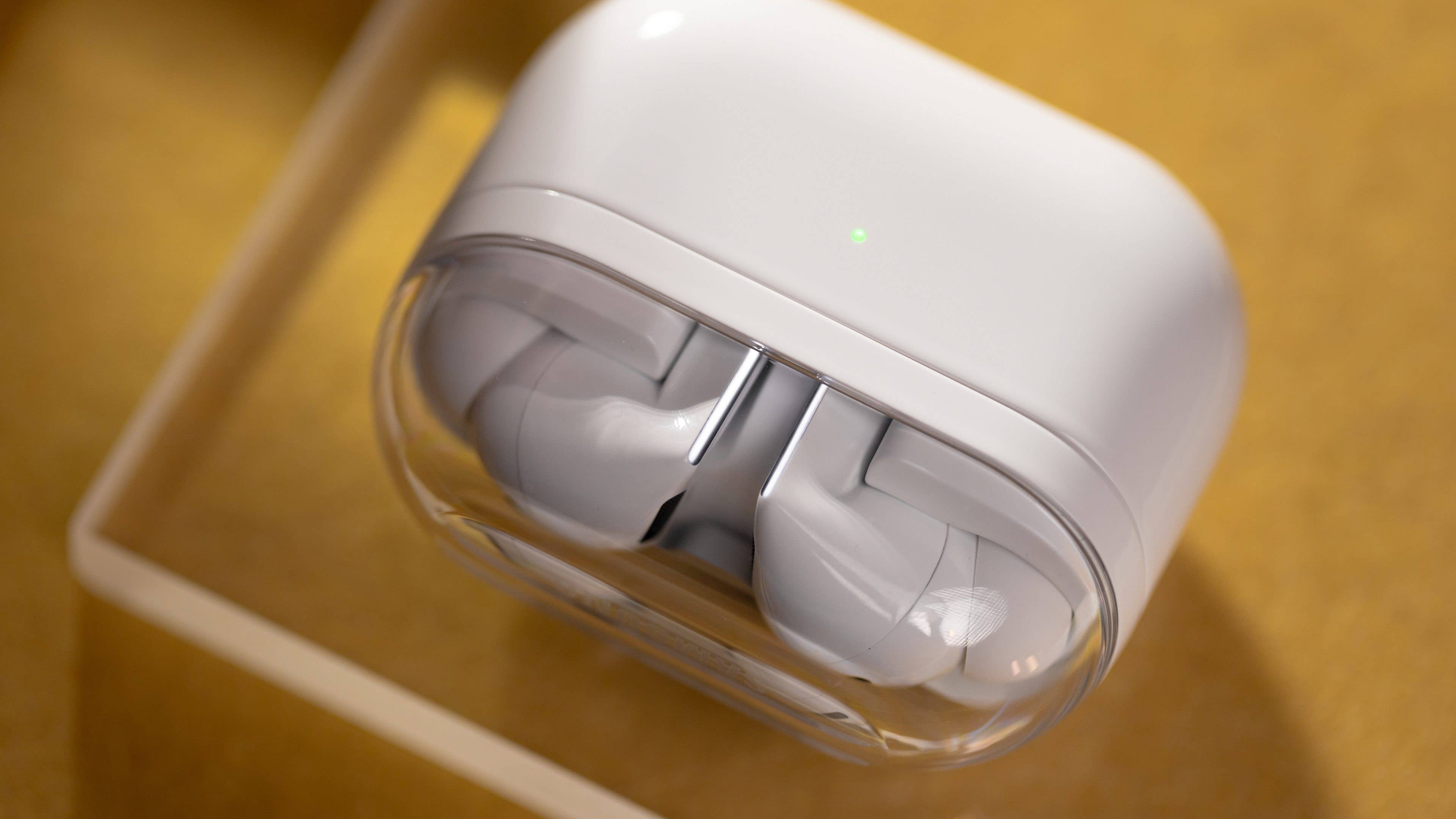 White wireless earbuds in a clear case on a yellow background.