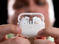 A person holding a white earbuds case with earbuds inside, focusing on the Samsung Galaxy Buds 3.