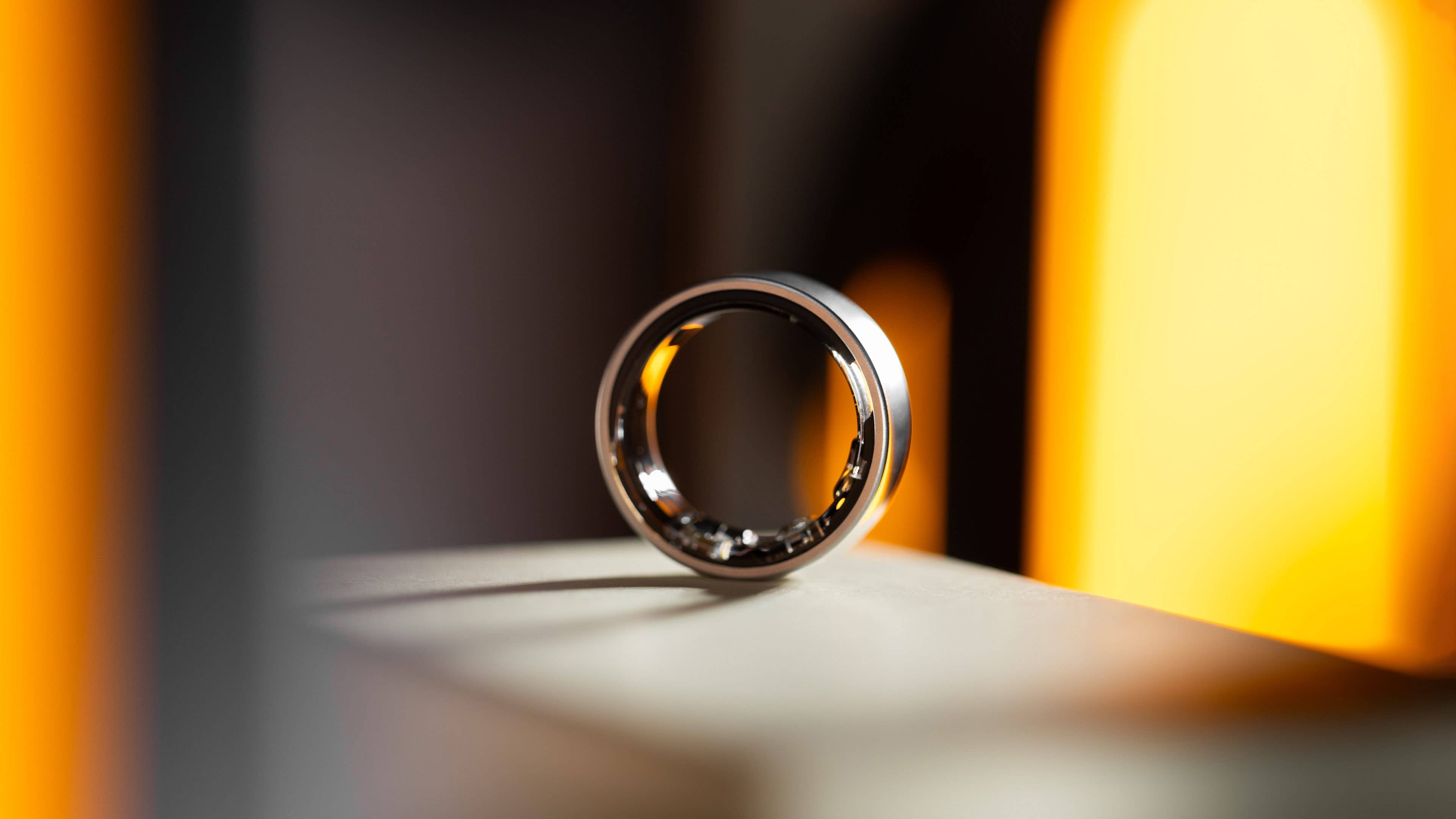 A sleek Samsung Galaxy Ring displayed on a surface with warm lighting in the background. A sleek Samsung Galaxy Ring displayed on a surface with warm lighting in the background.