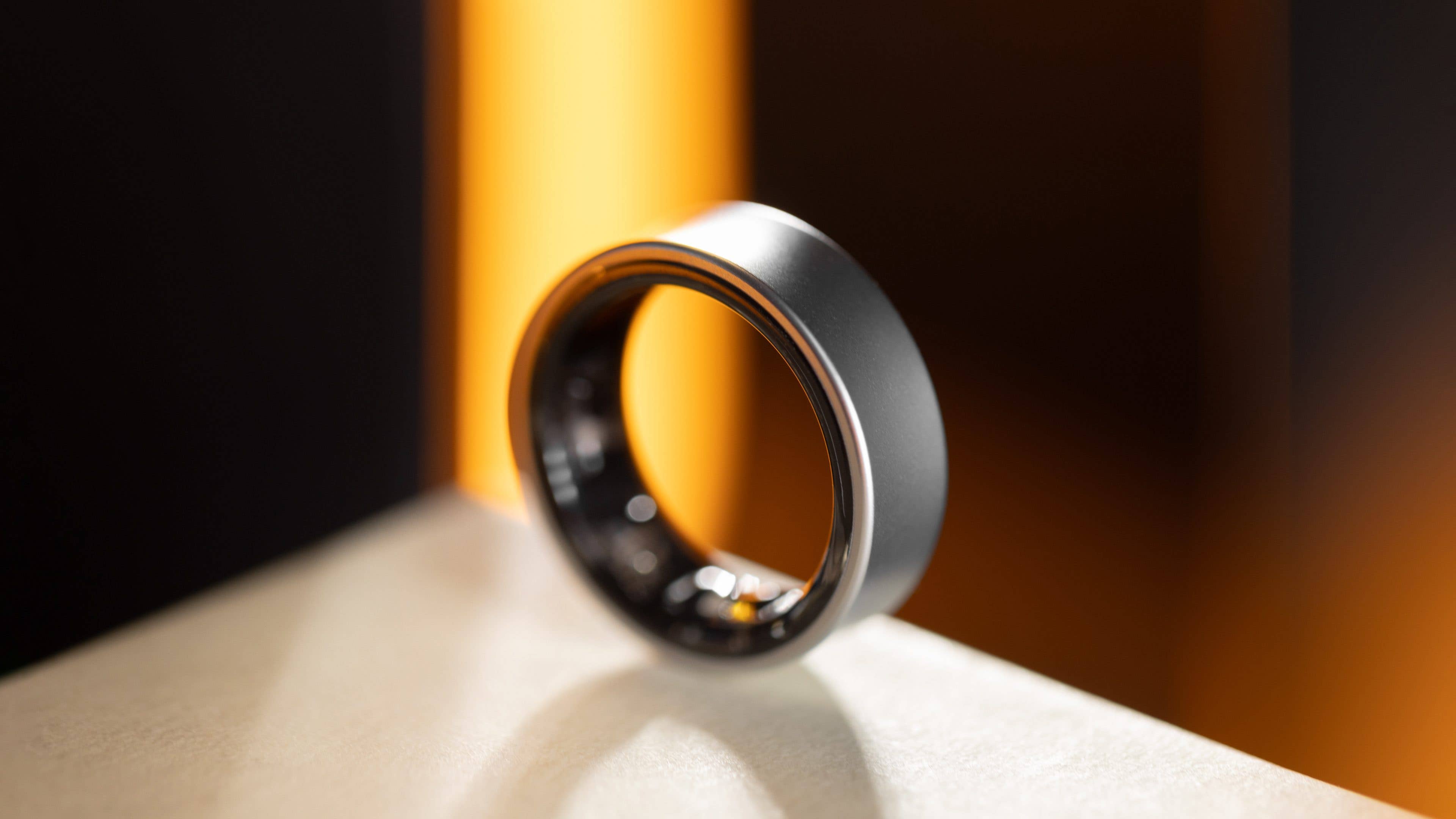 A sleek Samsung Galaxy Ring displayed on a surface with a blurred background. A sleek Samsung Galaxy Ring displayed on a surface with a blurred background.