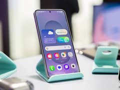 Samsung Galaxy S25 displayed on a teal stand with a colorful app interface.