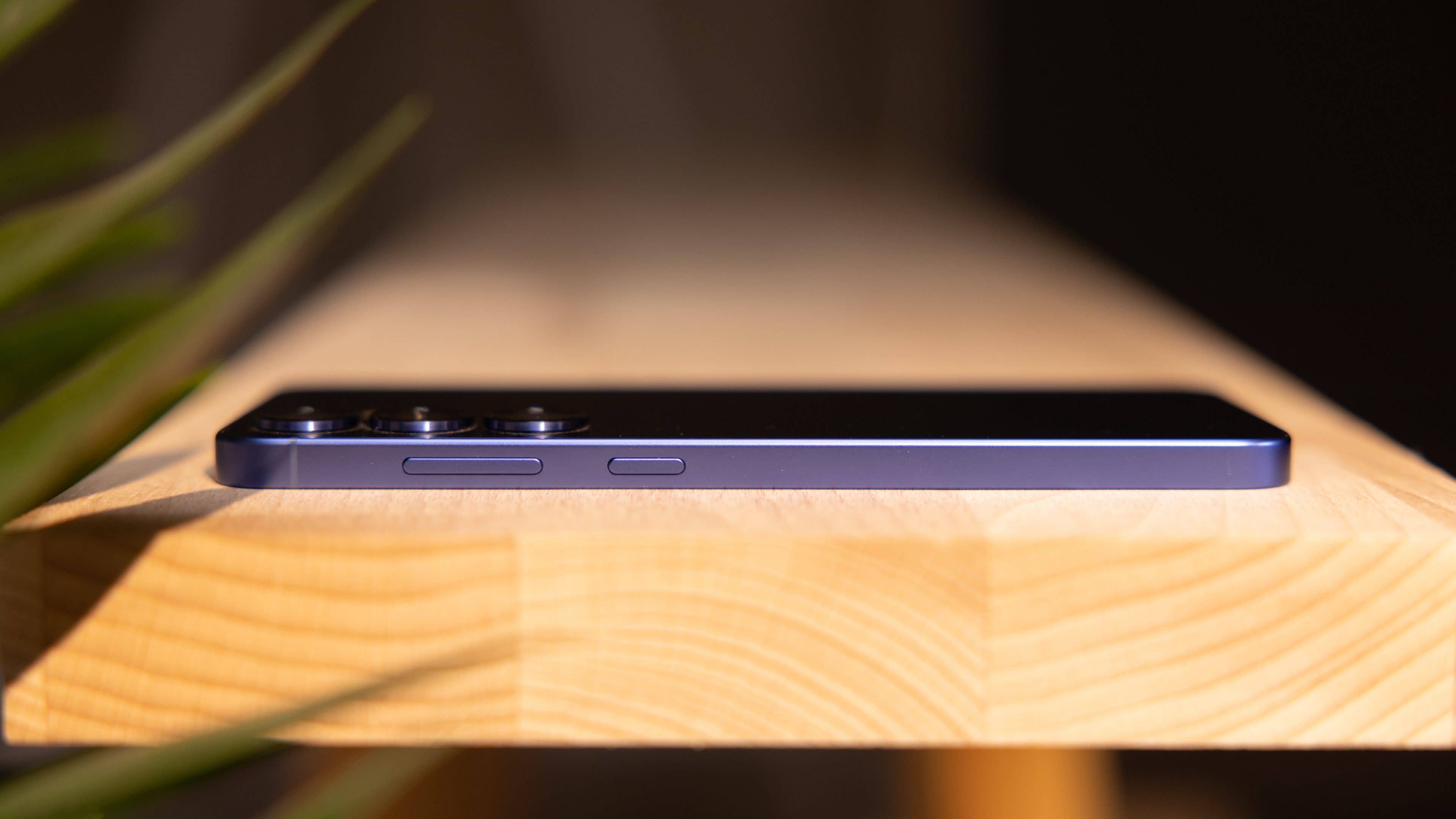 A Samsung Galaxy S25 Plus smartphone resting on a wooden surface, showing its slim profile and buttons.