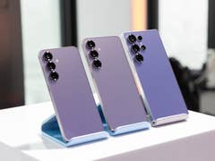 Three Samsung Galaxy S25 smartphones displayed on a stand, showcasing their sleek purple design.