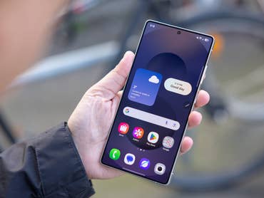 A person holding a Samsung Galaxy S25 Ultra smartphone displaying weather information and app icons.