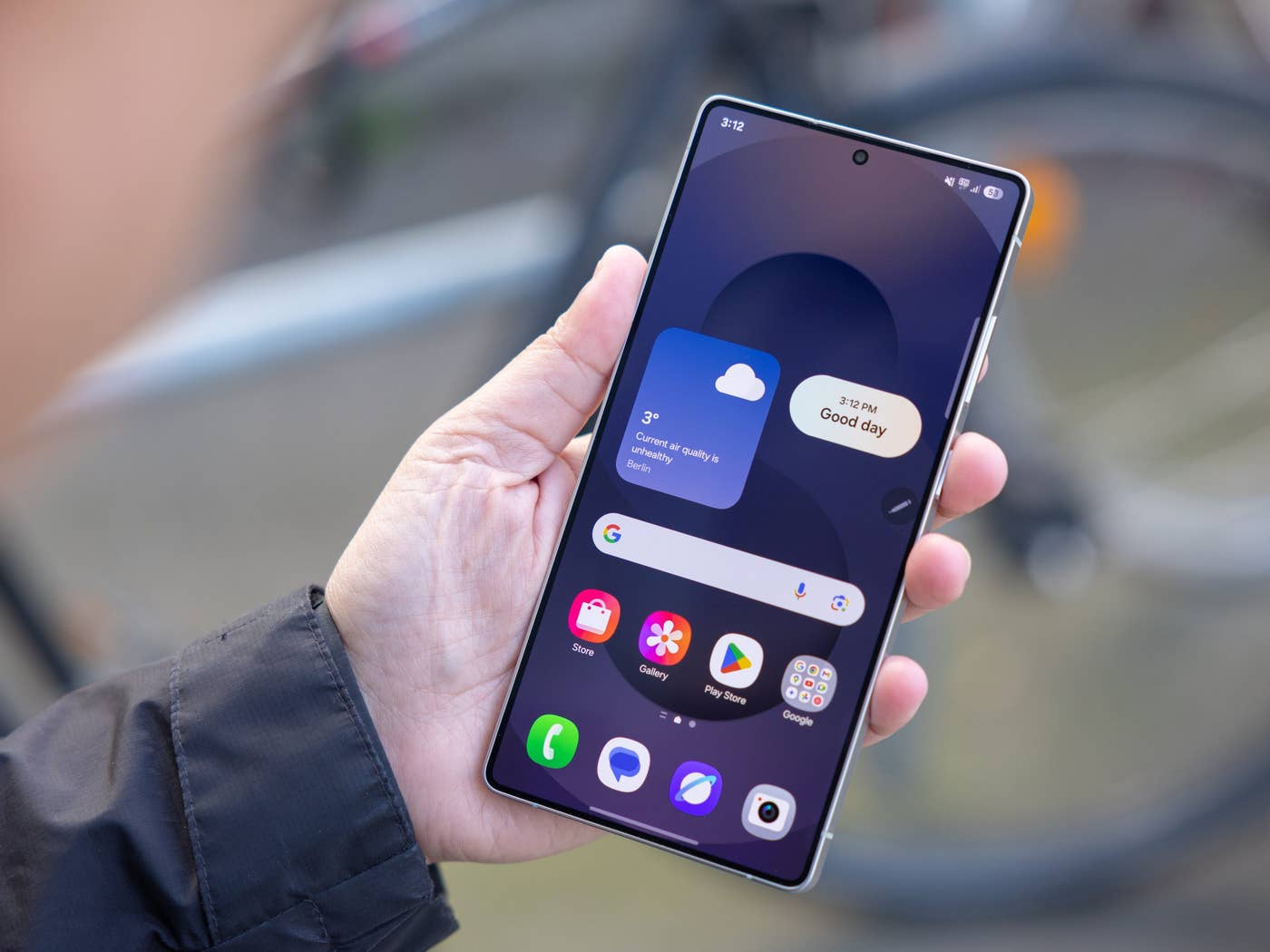 A person holding a Samsung Galaxy S25 Ultra smartphone displaying weather information and app icons.