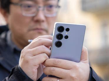 A man holding a Samsung Galaxy S25 Ultra smartphone, using its stylus, in an outdoor setting.
