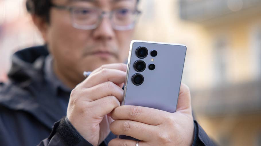 A man holding a Samsung Galaxy S25 Ultra smartphone, using its stylus, in an outdoor setting.