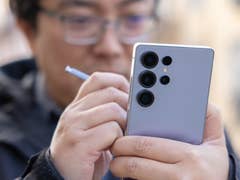 A person holding a Samsung Galaxy S25 Ultra smartphone with a stylus, focusing on the device's camera.