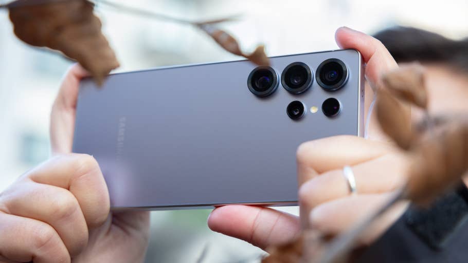 A person holding the back of a Samsung Galaxy S25 Ultra smartphone amidst dried leaves.