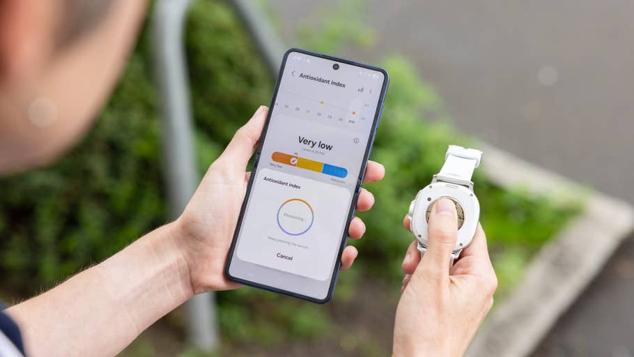 Person holding a Samsung Galaxy Watch 8 Classic while checking antioxidant index on a smartphone.