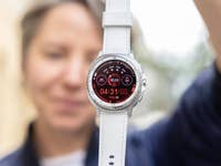 A person holding a Samsung Galaxy Watch 8 Classic, displaying a red interface with time and fitness stats.