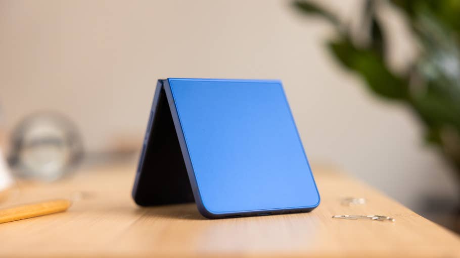 A blue Samsung Galaxy Z Flip 7 smartphone in a folded position on a wooden table.