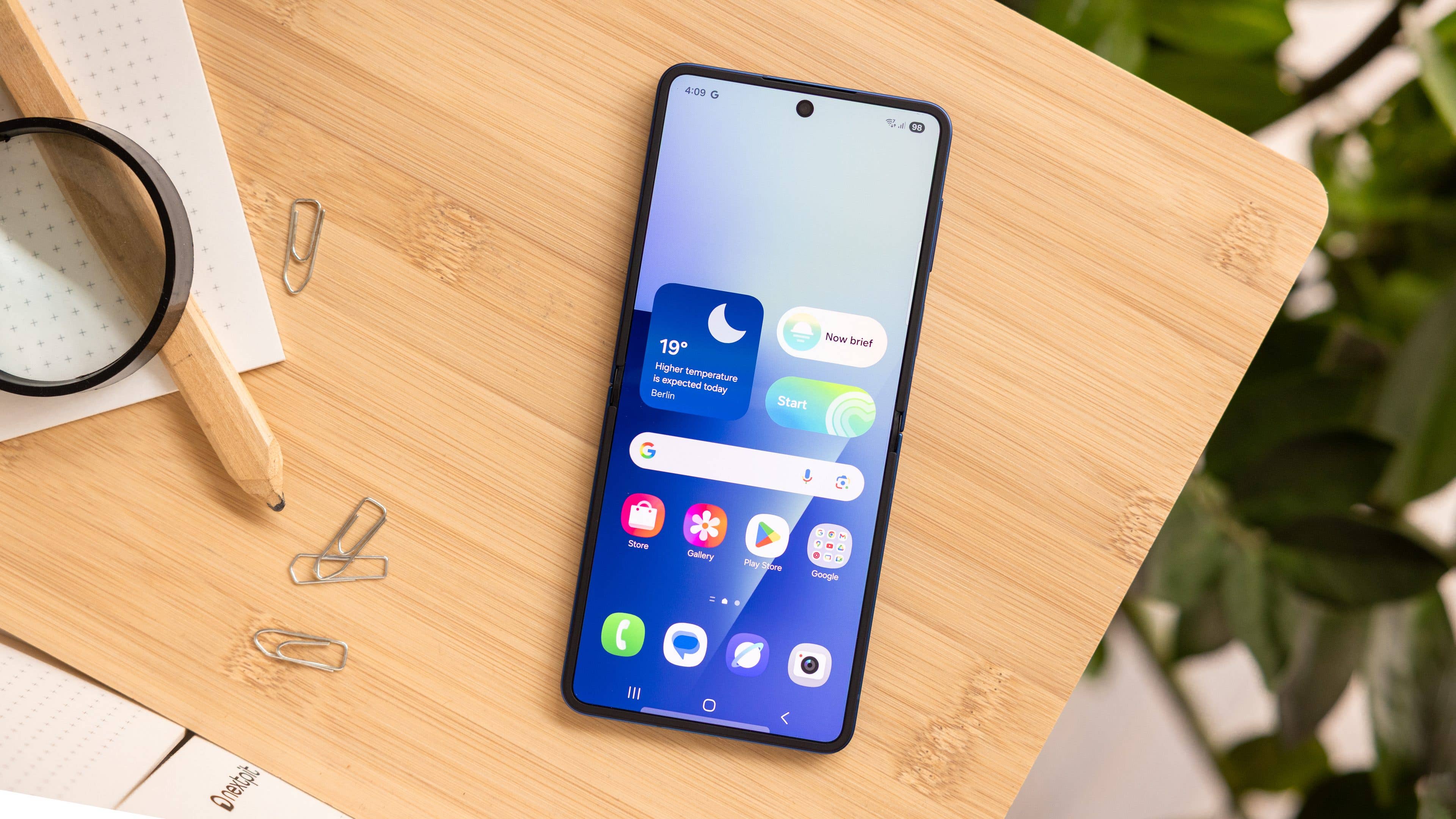Samsung Galaxy Z Flip7 smartphone on a wooden surface with app icons displayed on the screen.