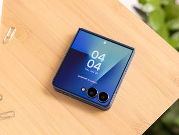 A Samsung Galaxy Z Flip7 smartphone on a wooden surface, displaying the time and date.