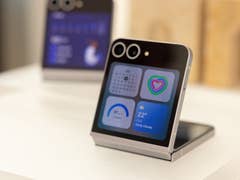 Samsung Galaxy Z Flip 6 smartphone displayed on a stand with a colorful screen showing weather and calendar.