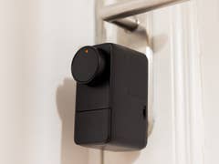 A black SwitchBot Lock Pro mounted on a door, featuring a circular dial and a small indicator light.