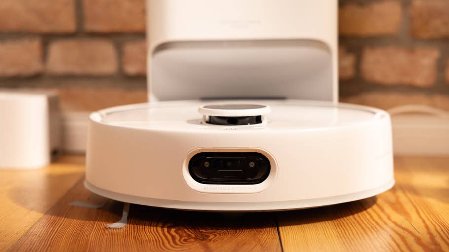 A white robot vacuum cleaner with AI obstacle avoidance on a wooden floor.