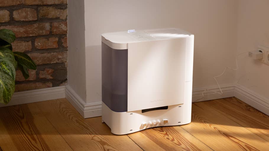 A SwitchBot S10 humidifier on a wooden floor next to a plant and a brick wall.