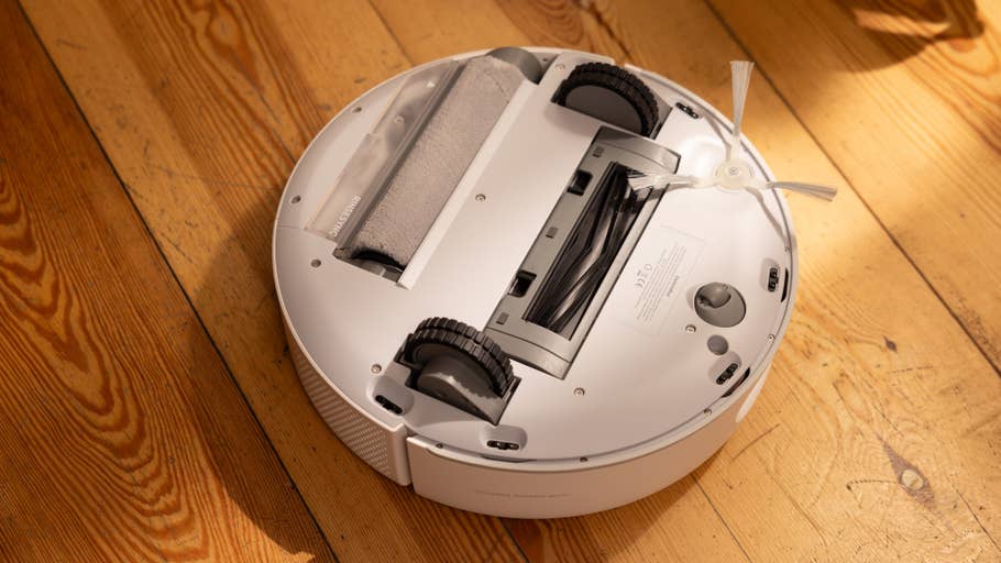 A white robot vacuum cleaner with visible brush attachment on a wooden floor.