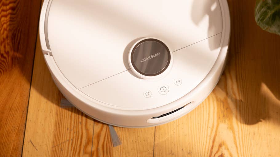 A white robot vacuum cleaner with LIDAR sensor on a wooden floor.