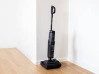 A Tineco Floor One S7 Stretch vacuum cleaner stands in a corner of a room on a wooden floor.