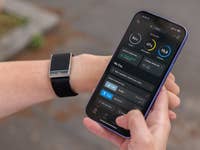 A person holding a smartphone displaying the Whoop app, with a fitness tracker on their wrist.