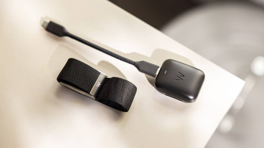 A black wearable device with a strap and a charging cable on a white surface.