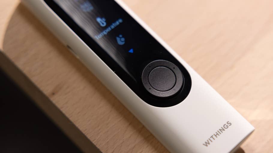 A Withings BeamO thermometer on a wooden surface showing a display with temperature reading.