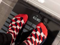 Feet with red and white patterned socks standing on a Withings Body Scan scale showing 62.80 kg.