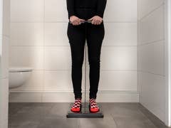 Person standing on a scale in a bathroom, holding a measuring tool.