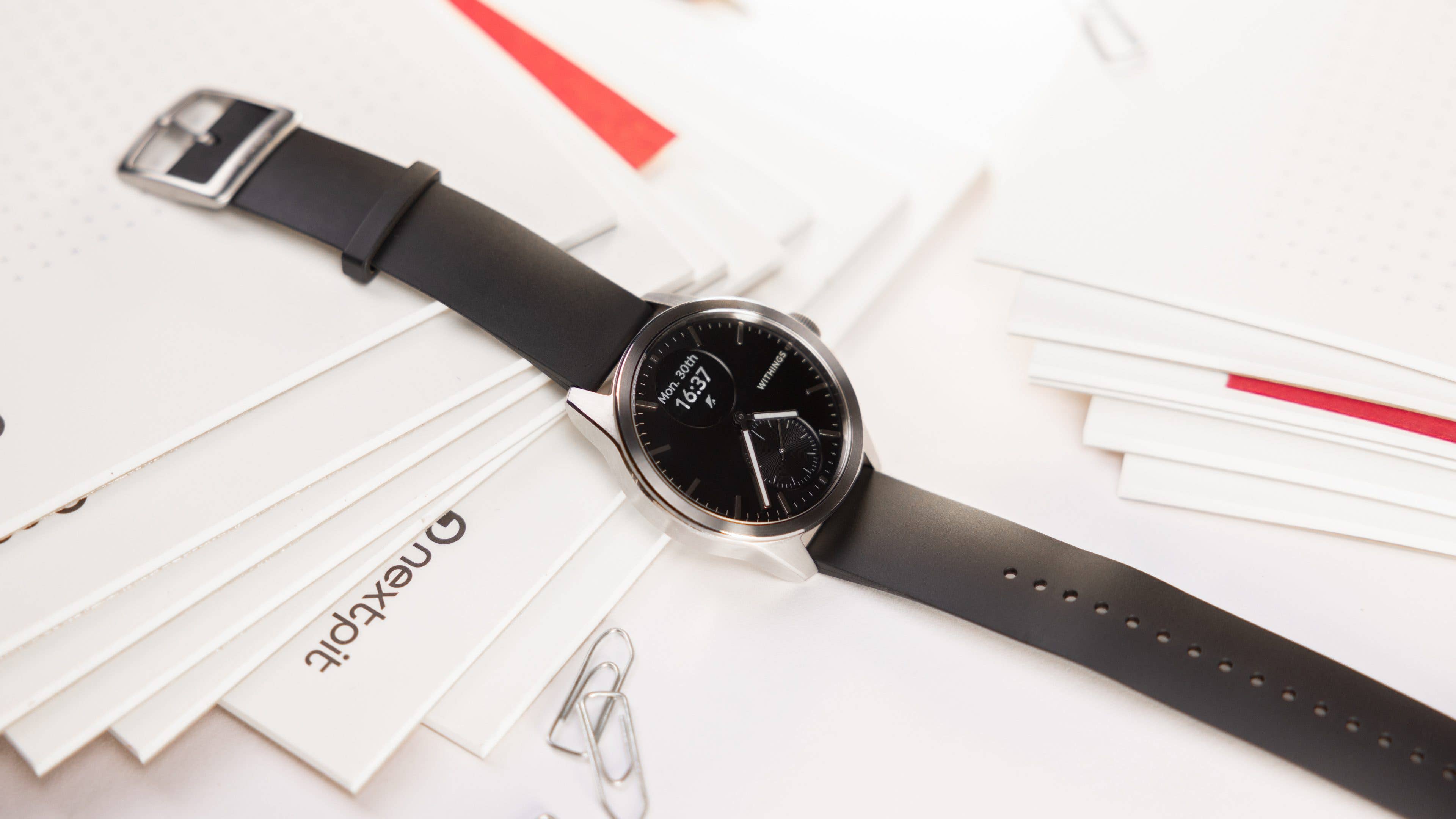 Withings Smartwatch 2 displaying the time in analog and digital forms, standing on a pile of paper leaves.