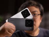 A person holding two Xiaomi 15 smartphones, one white and one black, with camera lenses visible.