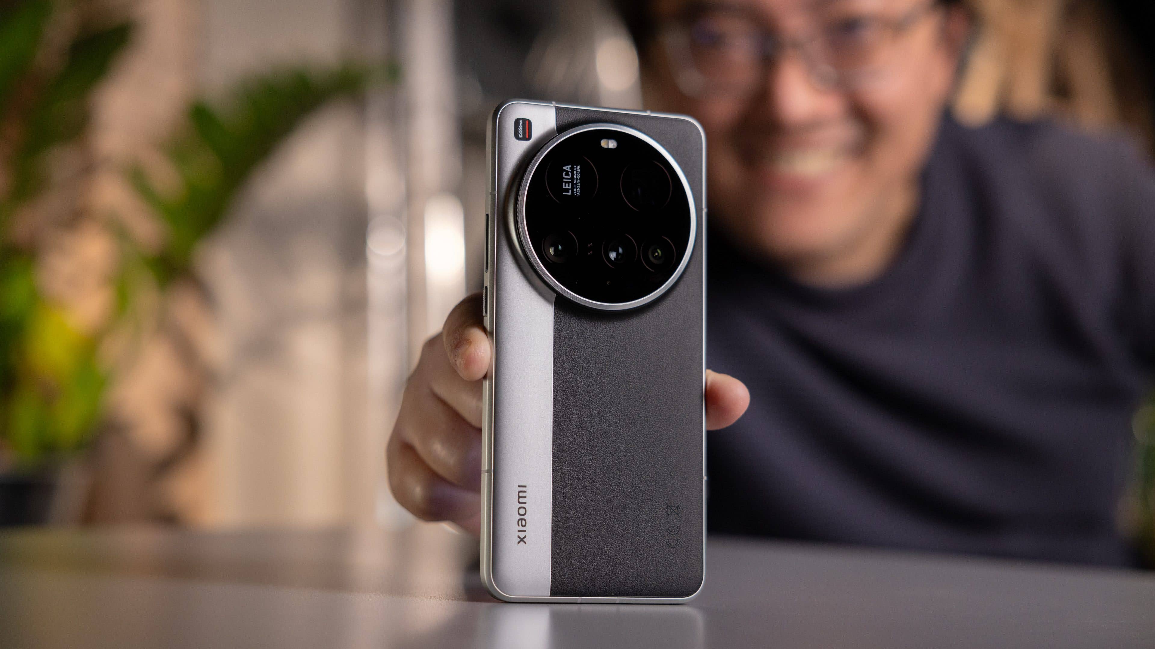 A person holding a Xiaomi 15 Ultra smartphone, smiling with greenery in the background. A person holding a Xiaomi 15 Ultra smartphone, smiling with greenery in the background.