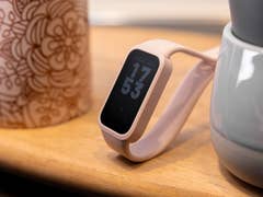 A Xiaomi Smart Band 9 Active in pink color displaying the time 17:53 on a wooden surface next to a patterned mug.
