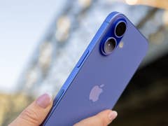 A person holding a blue Apple iPhone 16, showcasing the camera and side buttons.