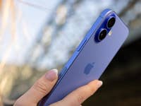 A person holding a blue Apple iPhone 16, showcasing its dual camera and sleek design.