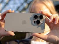 A person holding an iPhone 16 Pro facing the camera, showcasing its design and camera features.