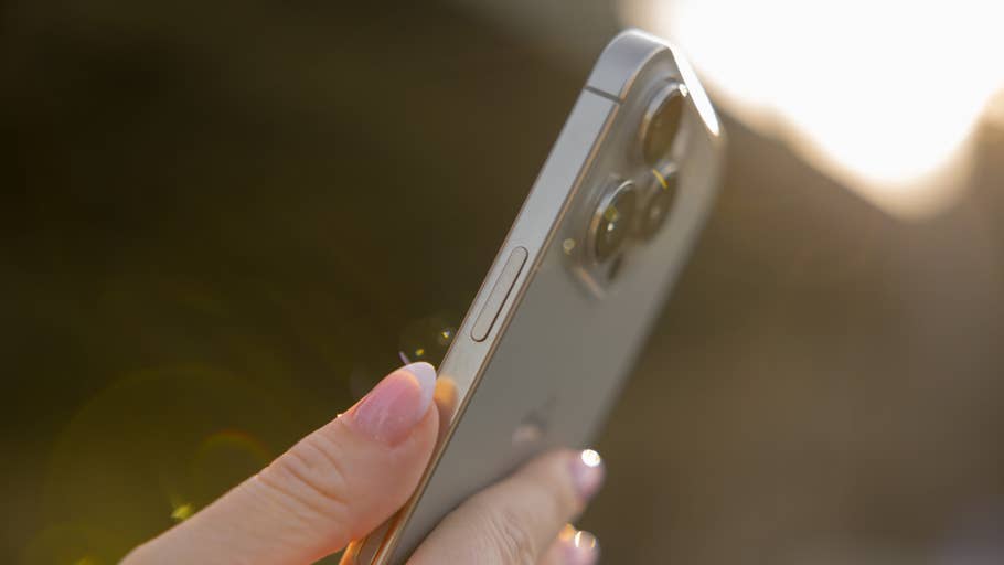A person holds an iPhone 16 Pro showing its camera and side buttons in sunlight.