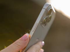 A person holding an iPhone 16 Pro, showcasing its camera and side buttons in sunlight.