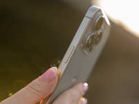 A person holding an iPhone 16 Pro, showcasing its camera and side buttons in sunlight.