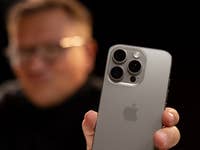 A person holds an Apple iPhone 16 Pro, showcasing its back design with three camera lenses.
