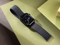 A black Apple Watch Series 10 on green and brown surfaces displaying various apps.