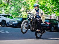 A person riding a motorcycle performing a wheelie on a street lined with parked cars.